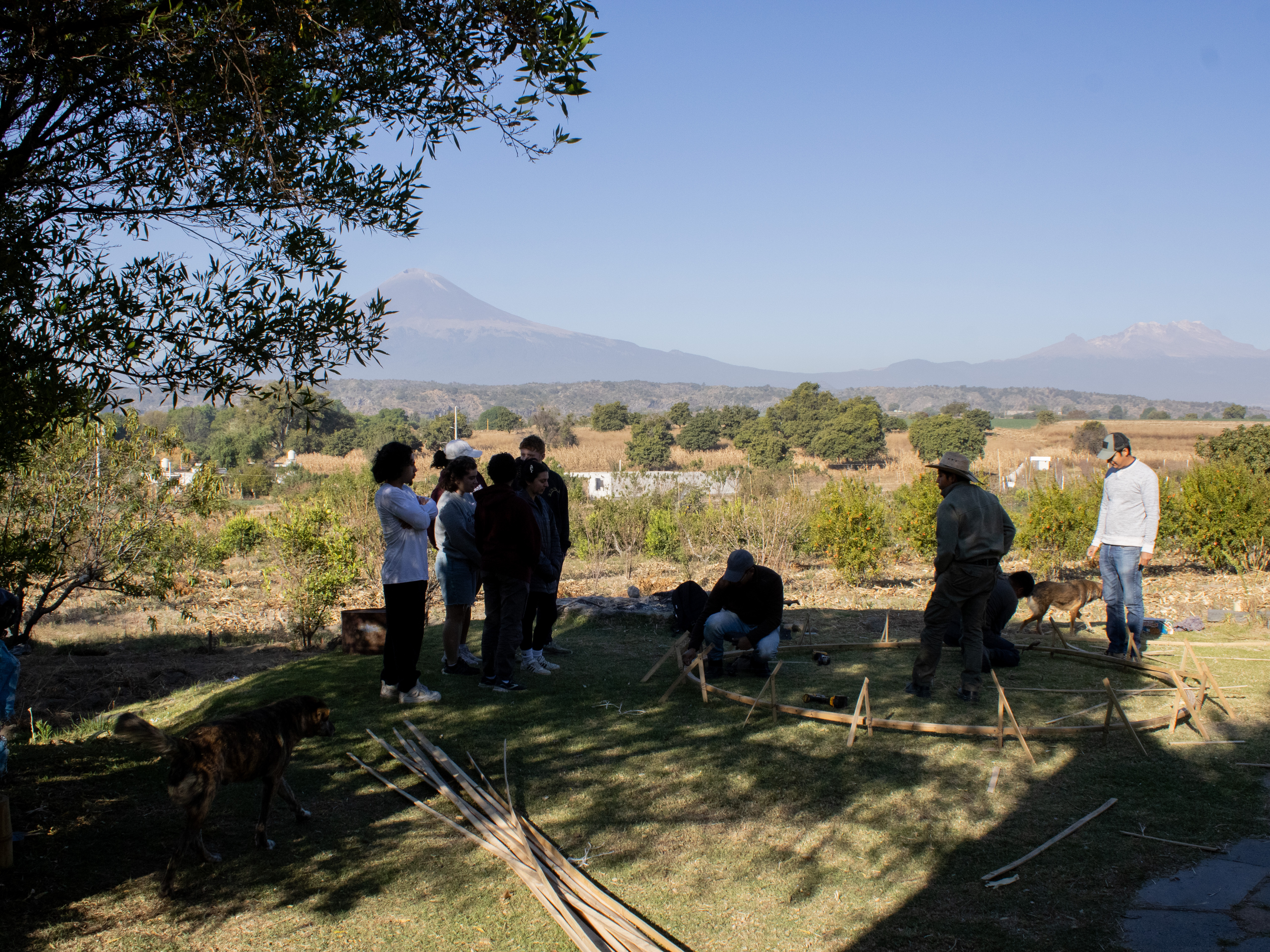 Students and local builders gathered around a bamboo structure with volcanoes on the horizon
