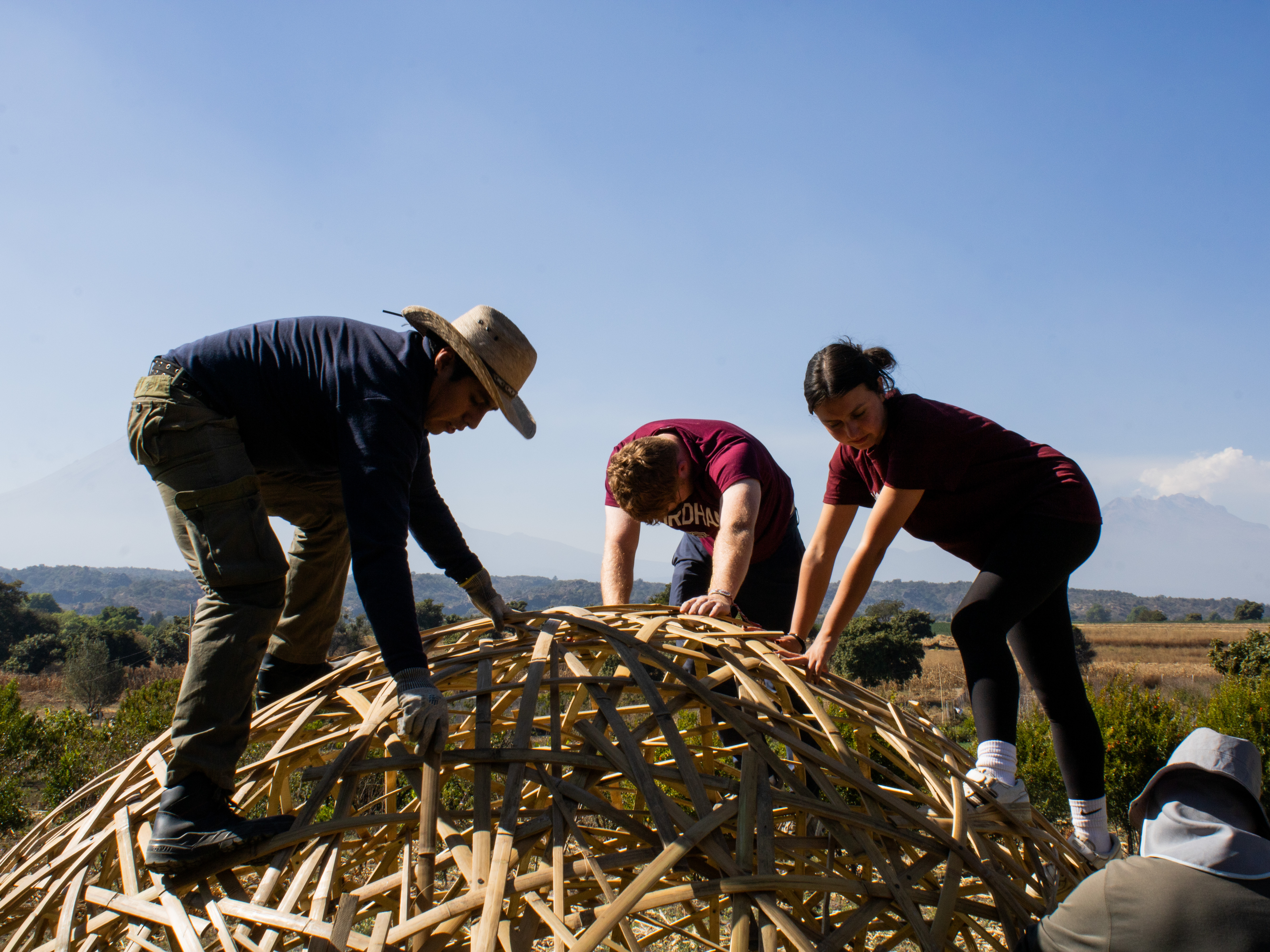 Volunteers and a local builder weaving a bamboo geodesic dome with a volcano in the distance
